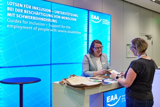Auf dem Bild ist eine EAA-Fachberaterin an dem Kongressstand der EAA zu sehen, die eine Interessierte über die Arbeit der EAA informiert.
