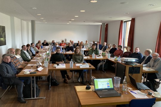 Gruppenfoto alle Teilnehmende des Workshops. Alle sitzen an ihren Tischen und lächeln in die Kamera.