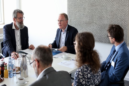 Mehrere Personen sitzen an einem Konferenztisch und unterhalten sich angeregt. 