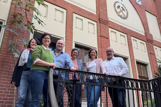 Auf dem Bild stehen fünf Teilnehmende von dem Workshop am Geländer vor einem Hauseingang. Auf dem Haus steht Glück auf über dem Bergwerkszeichen.