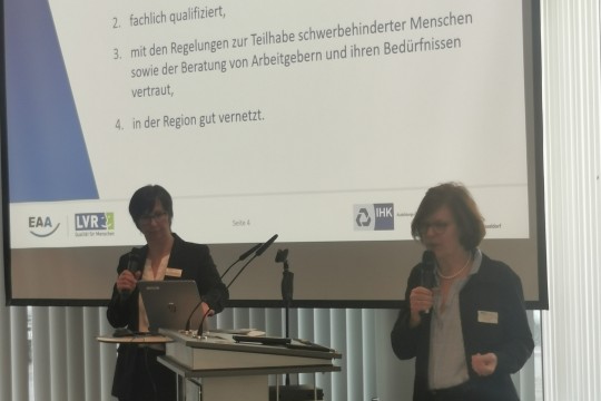 Das Bild zeigt zwei Fachberatenden der EAA Rheinland vor einer Power Point Präsentation zu der Arbeit der EAA