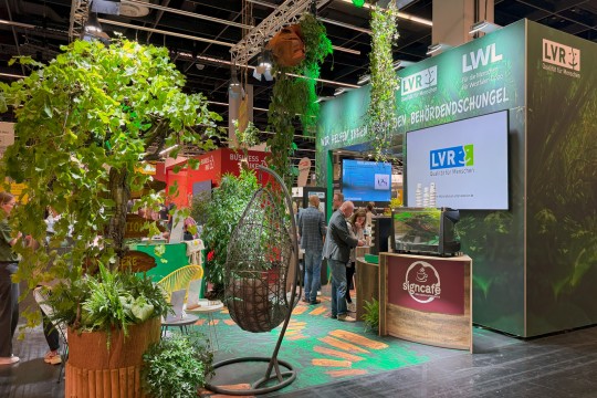 Auf dem Bild ist ein Messestand vom LVR und LWL mit vielen Pflanzen zu sehen. Der Slogan 
