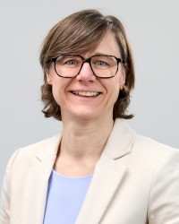 Potrait von Frau Geuke: Sie hat ihre dunkelbonden Haare zu einem Pferdeschwanz gebunden. Sie trägt eine langärmlige rosafarbende Bluse und lächelt in die Kamera.